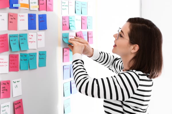 woman places post-it notes on an office wall as part of an agile ceremony